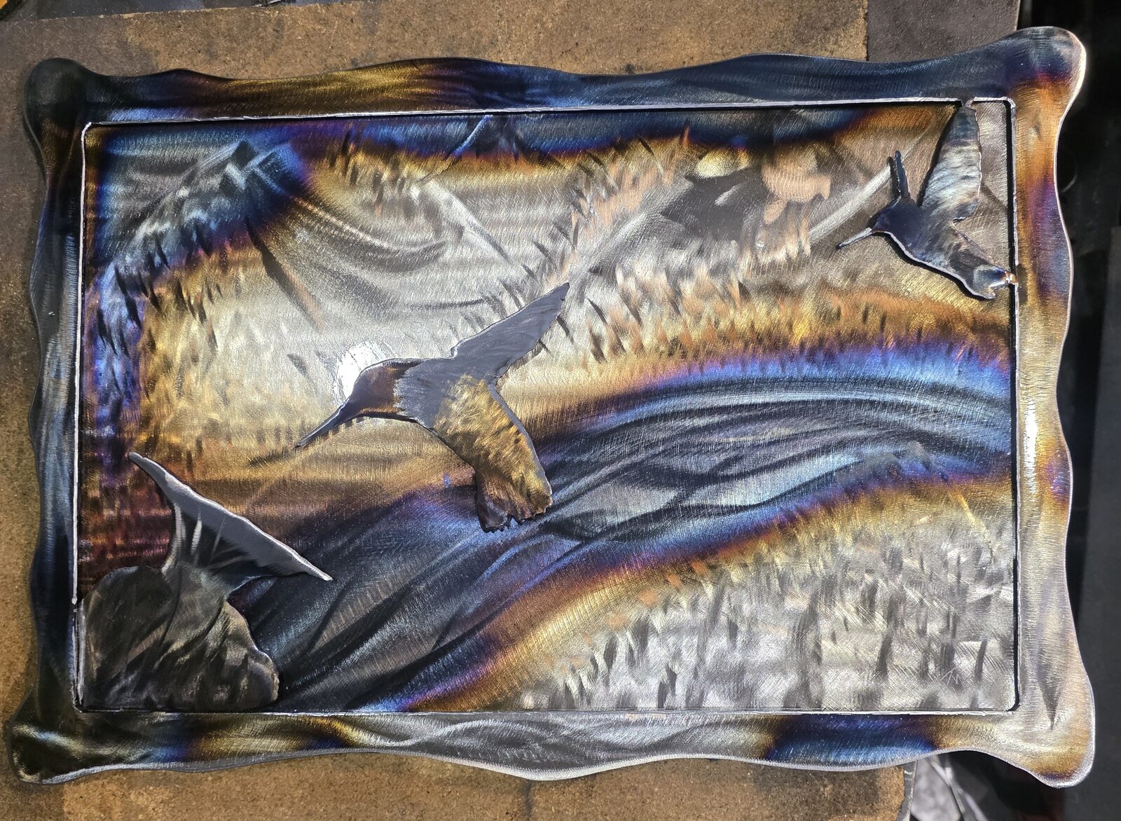 Heat-tinted steel wall art of hummingbirds over a mountain range